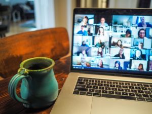 Photo thumbnails during a webinar displayed on a laptop screen next to a green coffee mug. 