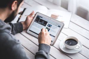 A man does online coursework on a tablet with a cup of coffee nearby. 