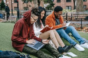 Two male and one female student laugh while studying on a lawn. 