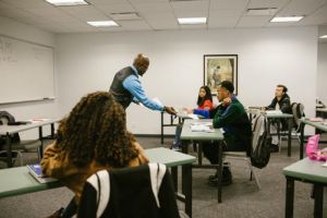 Several students receive instruction from a professor in a college classroom. 