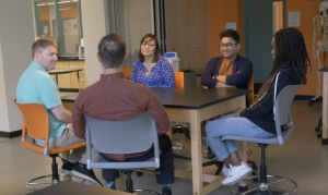 Five students in a meeting around a table in a science lab. 