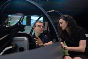 A photo of a woman demonstrating something in a cockpit of a plane