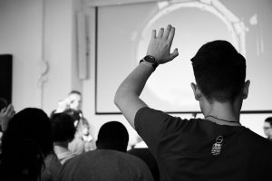 A black and white photo of the back of a student, raising their hand